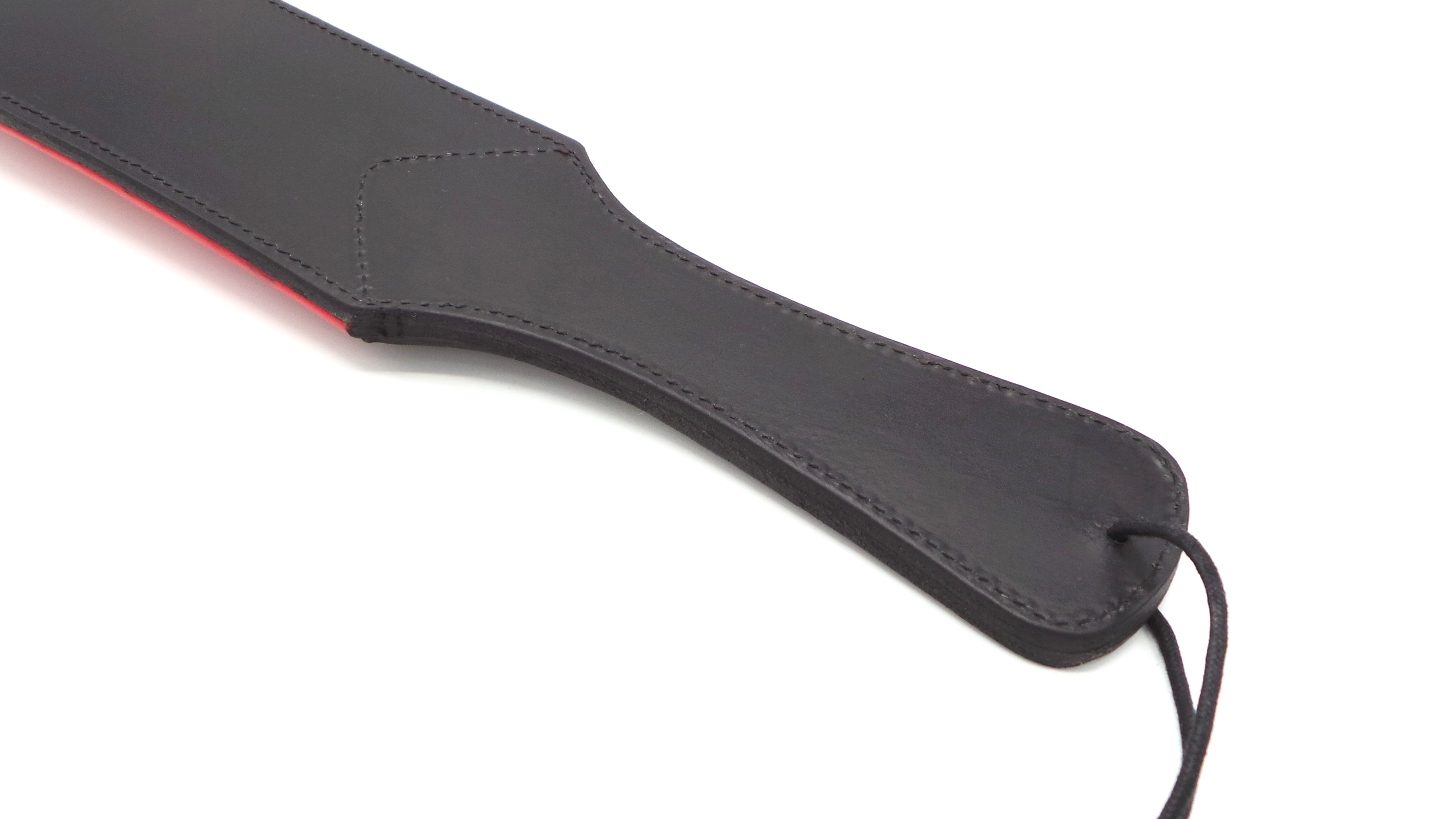 Nahaufnahme des schwarzen Ledergriffs eines BDSM-Paddels mit roter Rückseite und stabiler Handschlaufe.