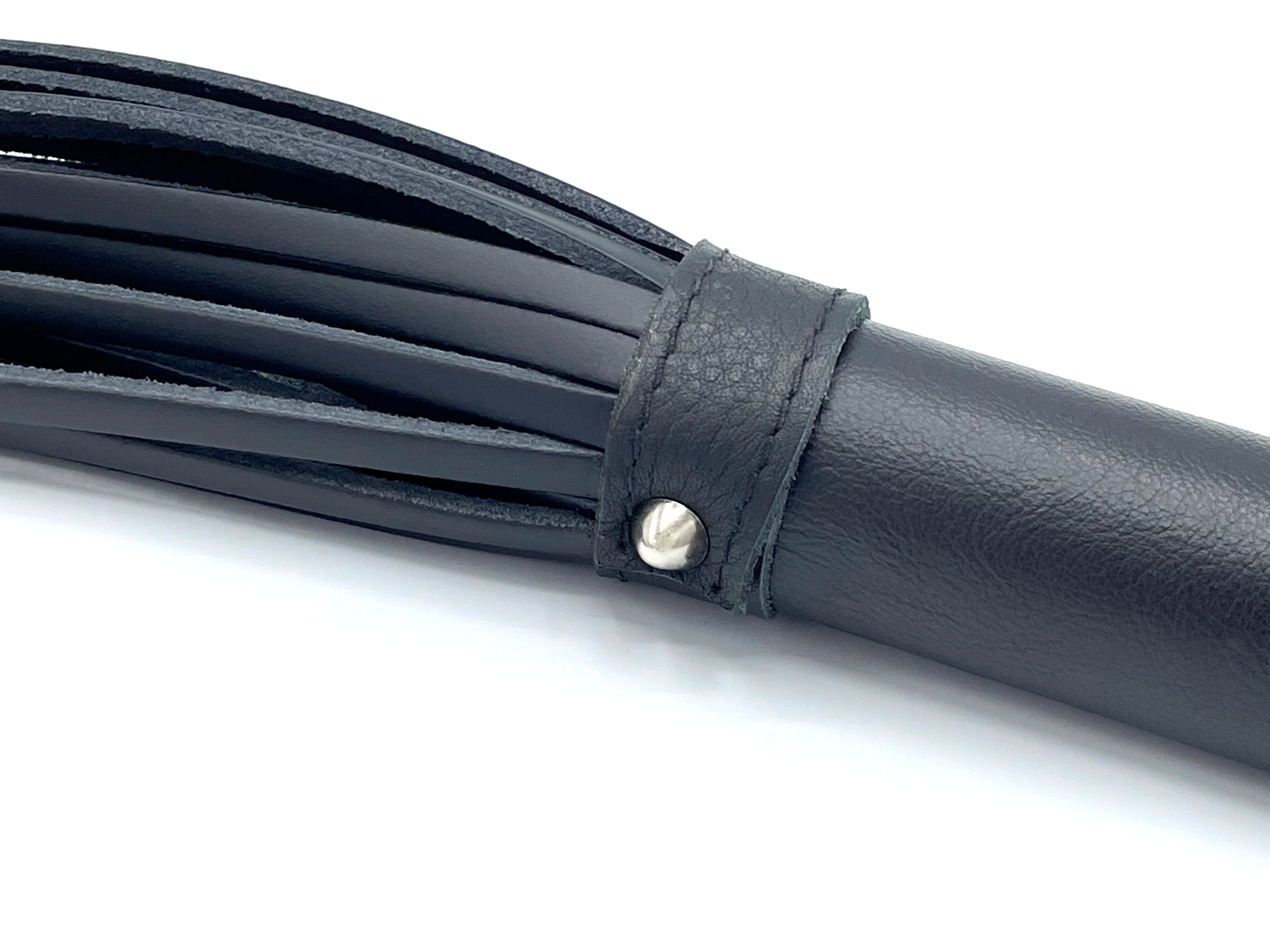 Detailaufnahme einer schwarzen Lederpeitsche mit genieteter Verarbeitung am Übergang von Griff zu Riemen.