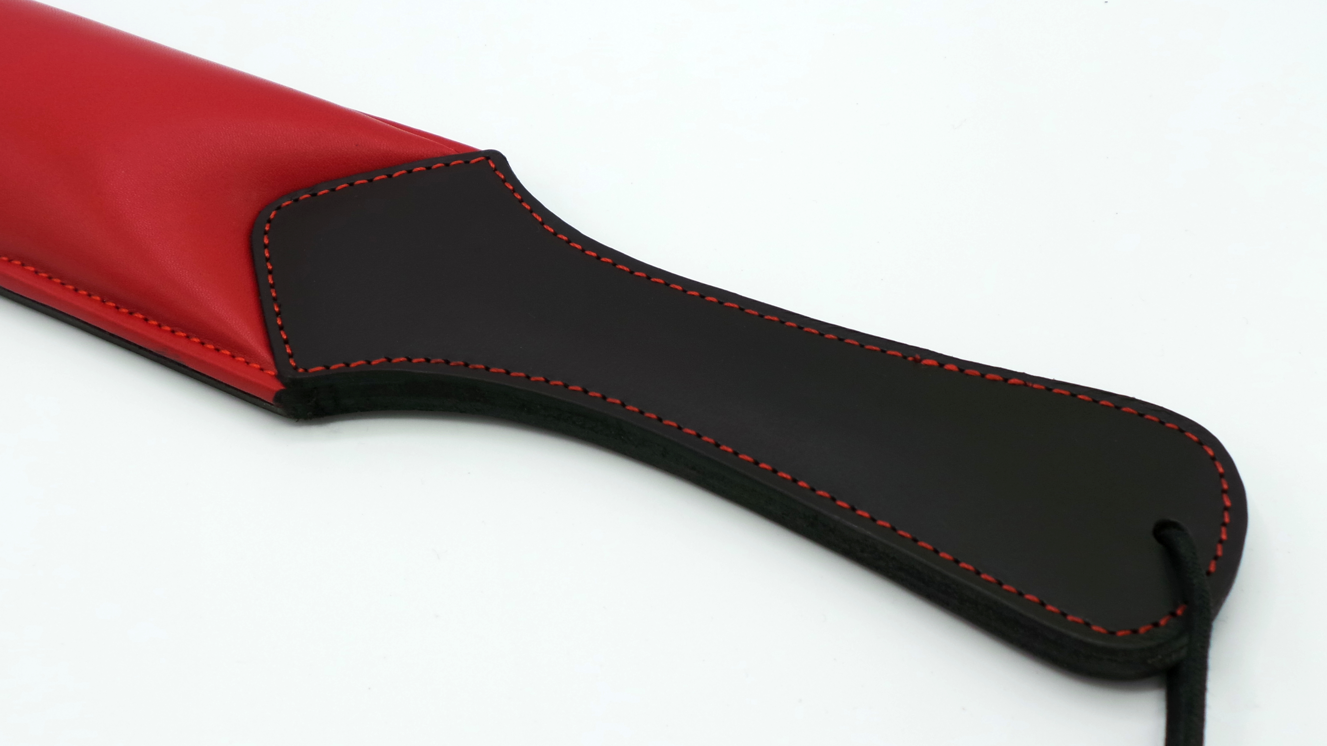 Detailansicht des Griffs eines gepolsterten Rindsleder-Paddels in Schwarz mit roter Ziernaht und roter Schlagfläche.